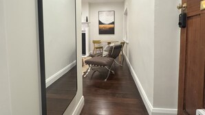 A hallway with a wooden floor, a large mirror on the left, a door with a brass handle on the right, and a dining area in the background with a table and chairs. - Discerning Accommodation in Thorndon (Wellington)
