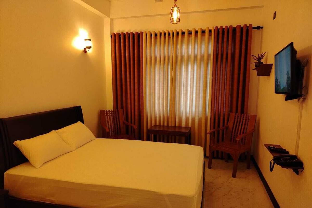 Una habitación de hotel con cama, escritorio, dos sillas, televisor y teléfono en la pared.
