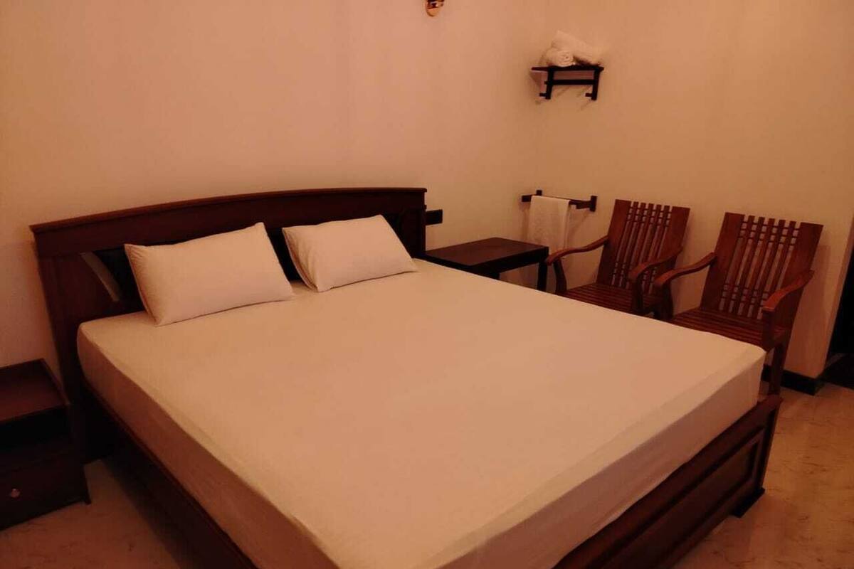 Una cama bien tendida con un cabecero de madera, una mesita de noche pequeña y dos sillas de madera.