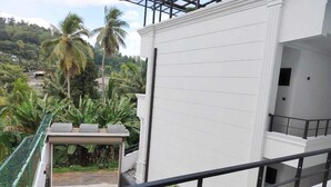 A white building with a balcony and a view of palm trees and greenery. - DIORA Hotel (Ratnapura)