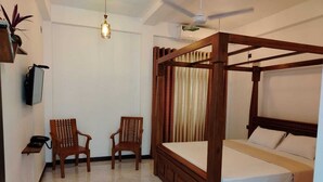 A four-poster bed with a wooden frame and white bedding, two wooden chairs, a small table with a phone, and a ceiling fan. - DIORA Hotel (Ratnapura)