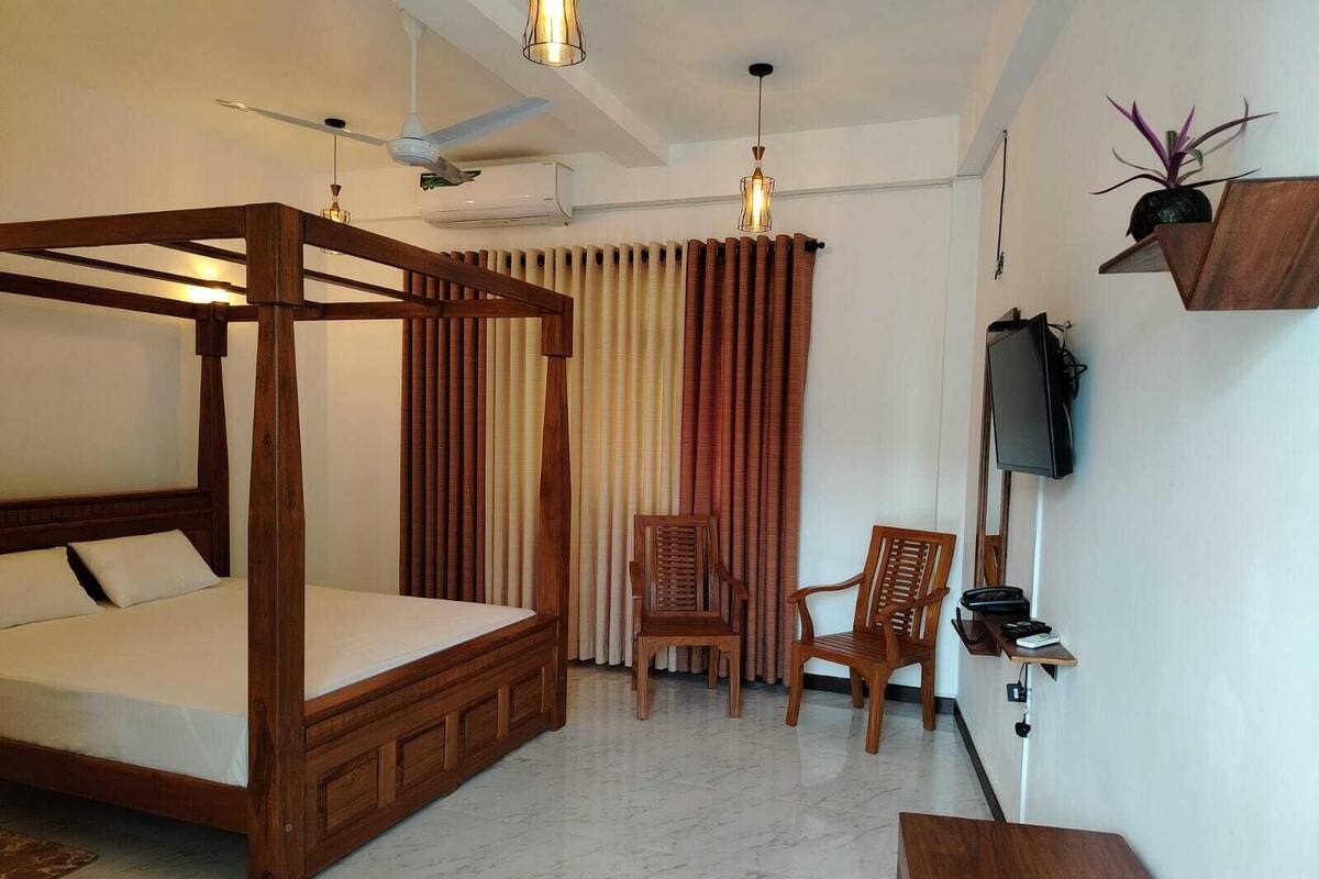 Un dormitorio con cama con dosel, dos sillas de madera, un televisor montado en la pared y un ventilador de techo.