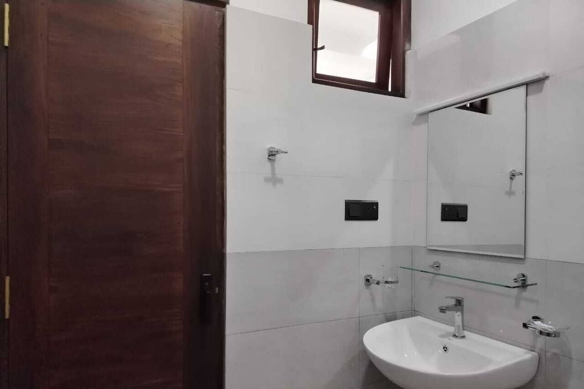 Un baño con puerta de madera, un lavabo blanco, un espejo y una ventana pequeña.