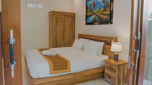 Een netjes opgemaakt bed met een houten hoofdbord, een nachtkastje met een lamp, en een schilderij aan de muur.