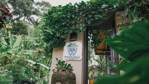 Naamplaatje voor Twins Bali House, met een stenen gezichtsbeeldhouwwerk en weelderige begroeiing.