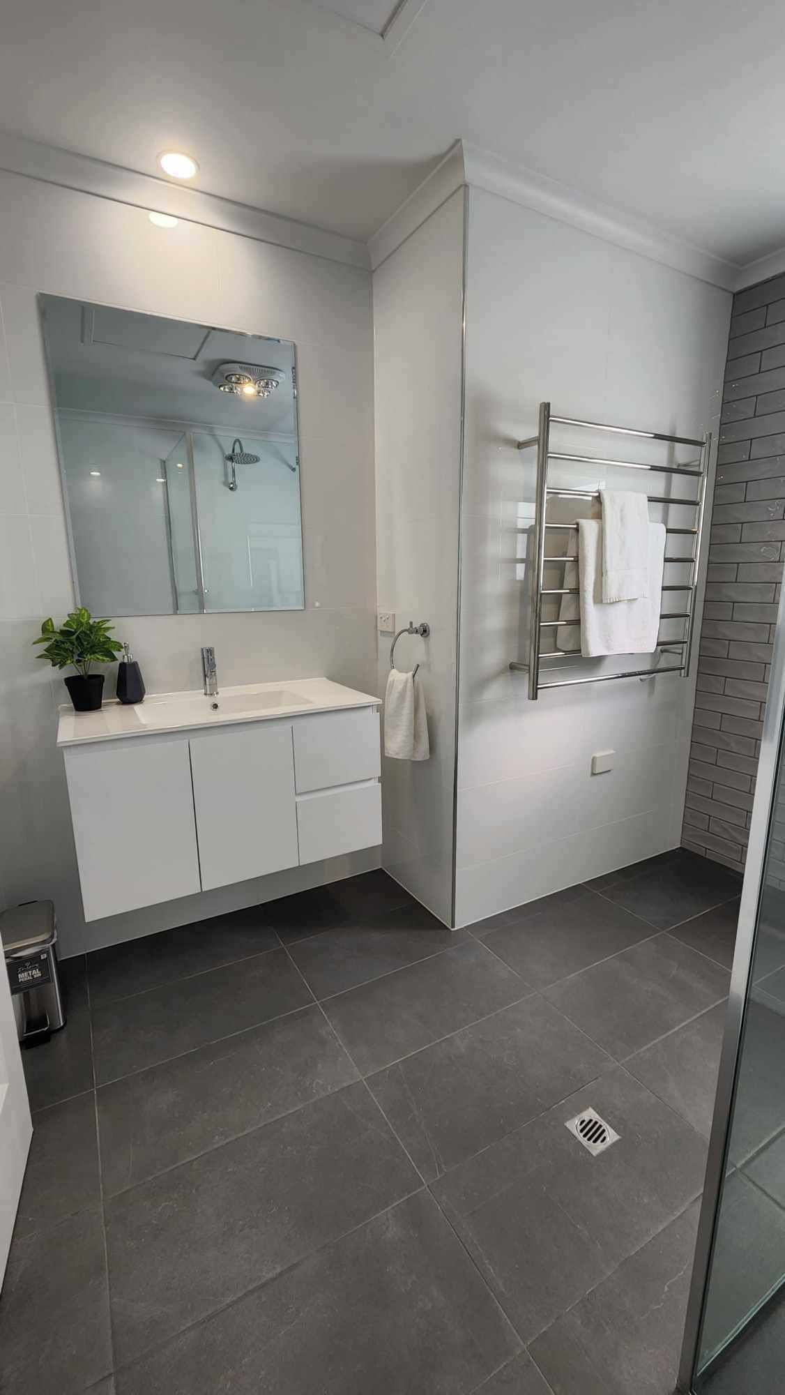 Une salle de bain moderne avec une douche à parois de verre, un meuble-lavabo blanc et un porte-serviettes.