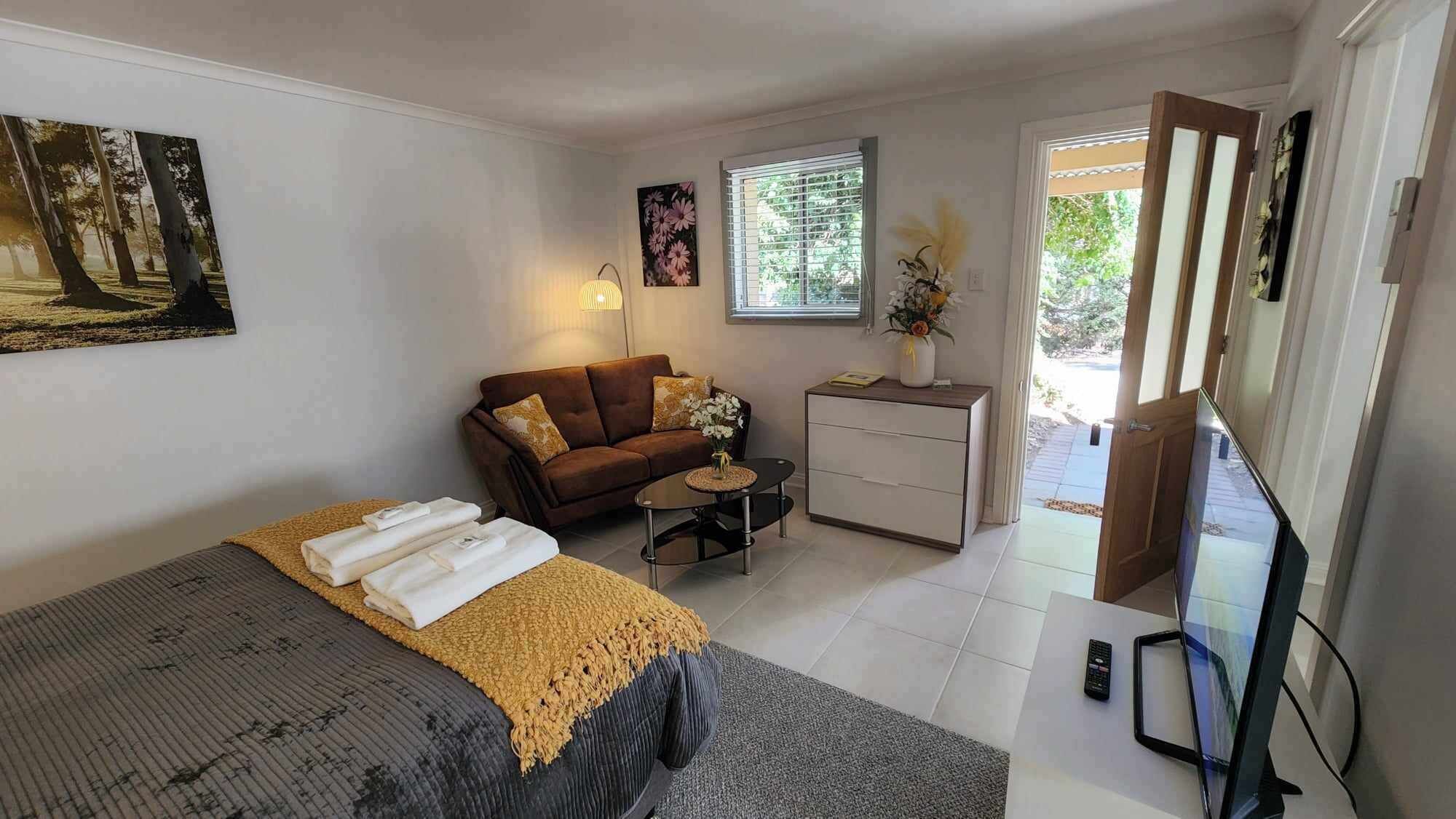 Quarto com cama, sofá, mesinha, escrivaninha e televisão.