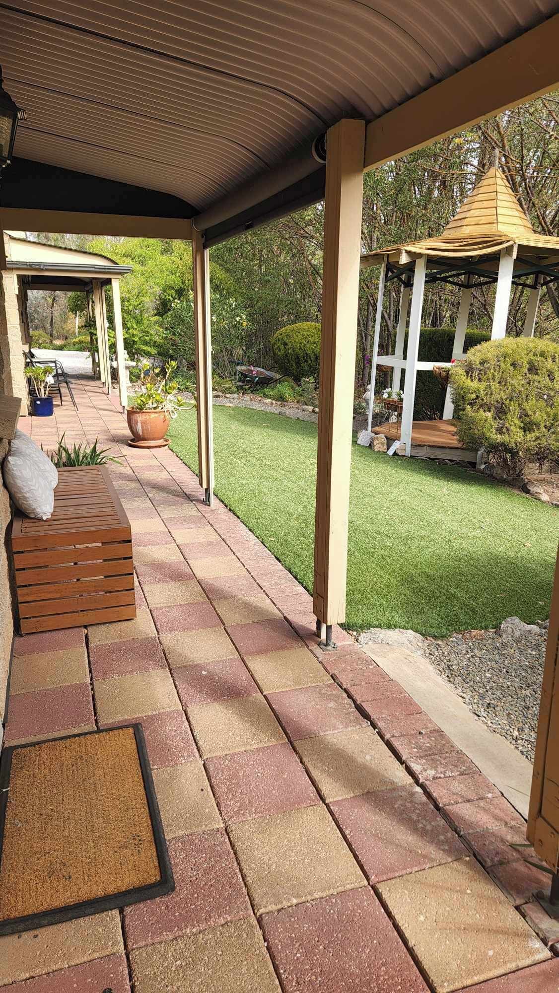 A covered patio area with a wooden bench, a small table, and a pergola structure.