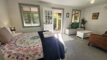 A bedroom with a bed, a desk, a TV, and a door leading to an outdoor area.