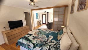 Un dormitorio con cama, televisión, cómoda y una puerta corredera que da a un baño.