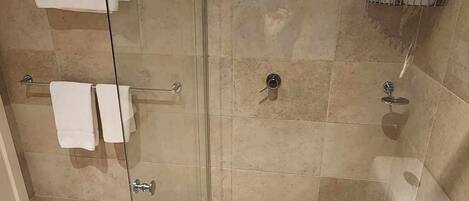 A glass-enclosed shower stall with a showerhead, a towel rack with folded towels, and a small shelf with toiletries.