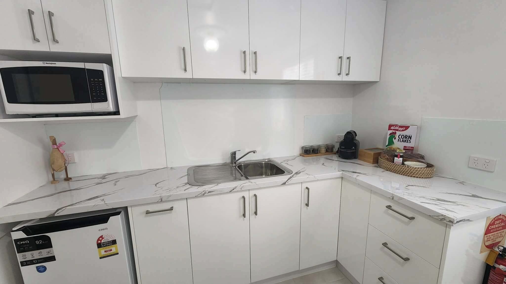 A kitchen with white cabinets, a microwave, a sink, and a coffee maker.