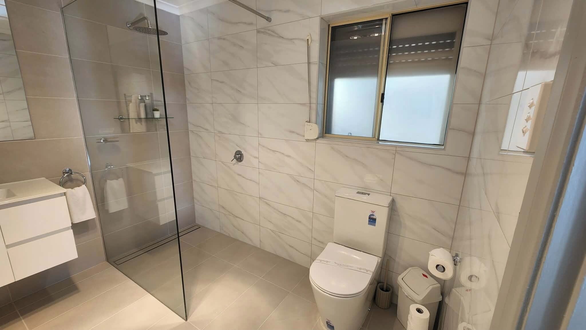 A modern bathroom with a glass shower enclosure, a toilet, and a small window.