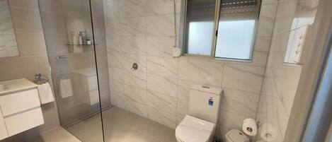 A modern bathroom with a glass shower enclosure, a toilet, and a small window.