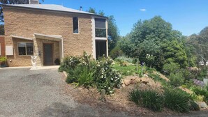 Un edificio de dos pisos de piedra con un camino de grava y un jardín ajardinado con diversas plantas y flores.