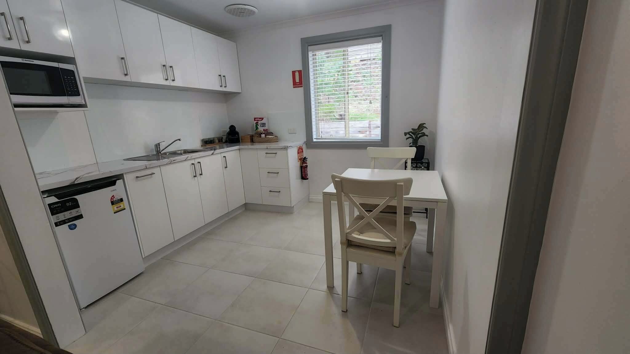 A kitchen with white cabinets, a microwave, a sink, and a window with blinds.