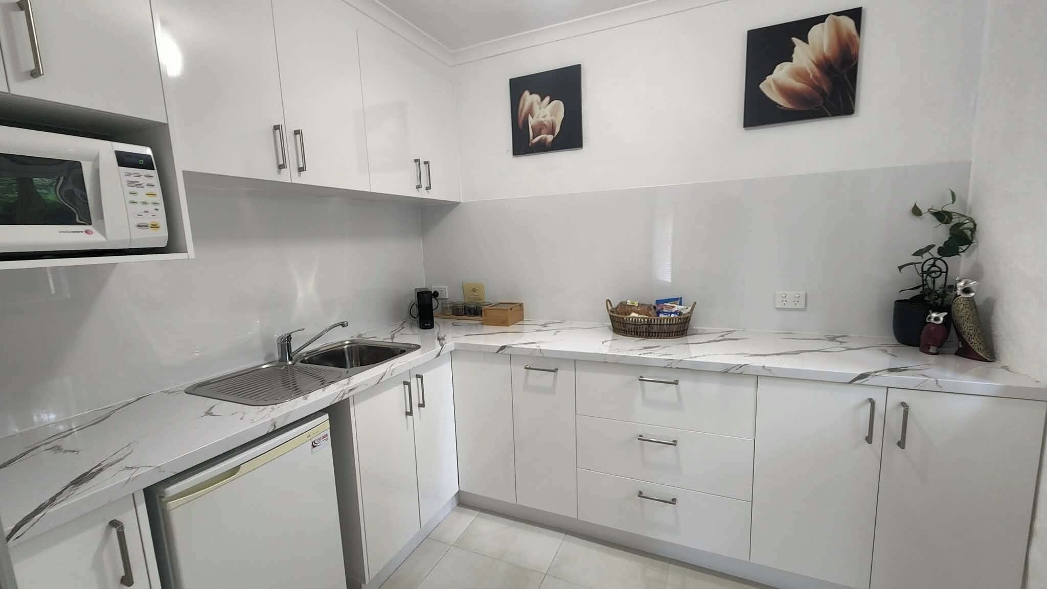 A modern kitchen with white cabinets, a built-in microwave, a sink, and two wall-mounted flower paintings.