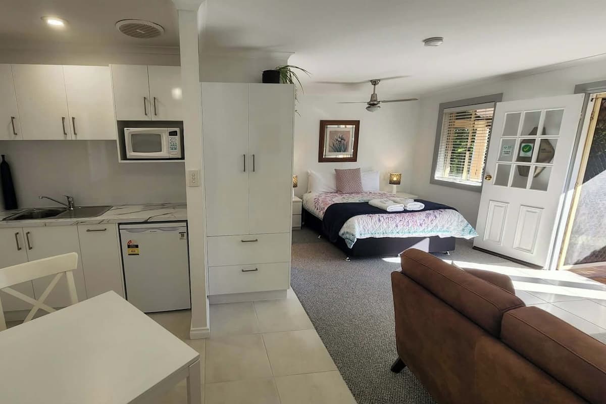 Une chambre d’hôtel compacte dotée d’une kitchenette, d’un lit recouvert d’une courtepointe à motifs floraux, d’un ventilateur de plafond et offrant une vue sur l’extérieur.