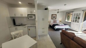 Habitación de hotel pequeña con kitchenette, cama con colcha estampada, ventilador de techo y vistas al exterior.