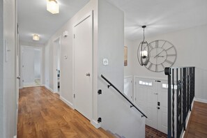 A hallway with wooden flooring, white doors, a staircase with a handrail, and a wall-mounted clock.
