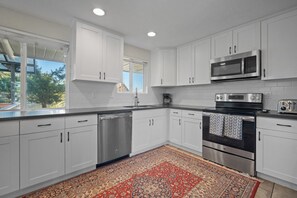 A modern kitchen with white cabinets, stainless steel appliances, and a patterned rug.