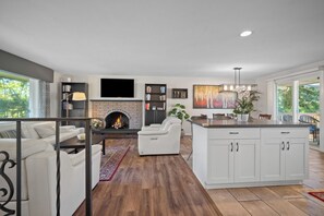 A modern living room with a fireplace, a flat-screen TV, and a dining area with a large island.