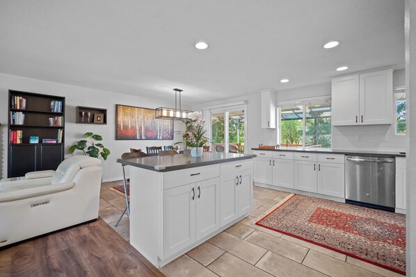 A modern kitchen with white cabinets, a stainless steel refrigerator, and a dining area with a white sofa and a dining table.