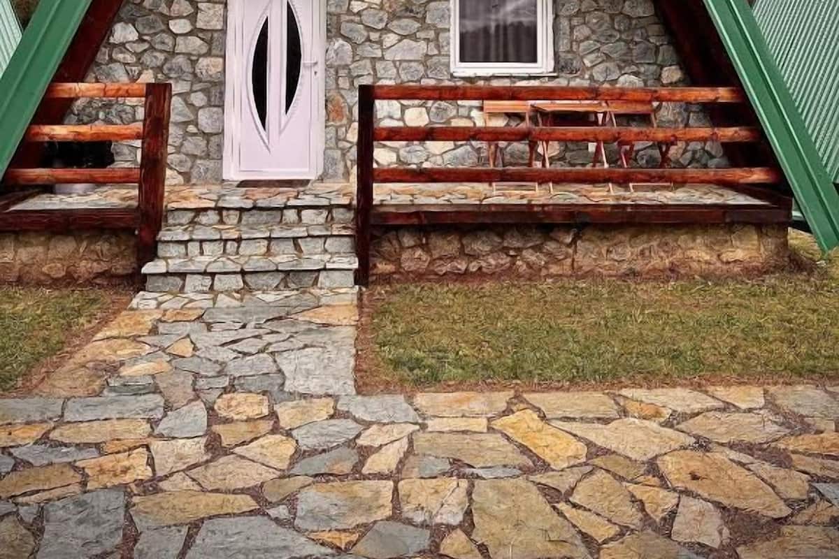 A stone cottage with a wooden roof, a stone foundation, and a green roof.