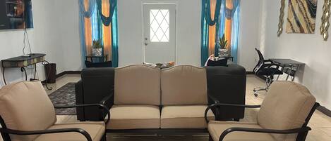 Sala de estar con un sofá, dos sillones, una mesita, televisor y cortinas decorativas.