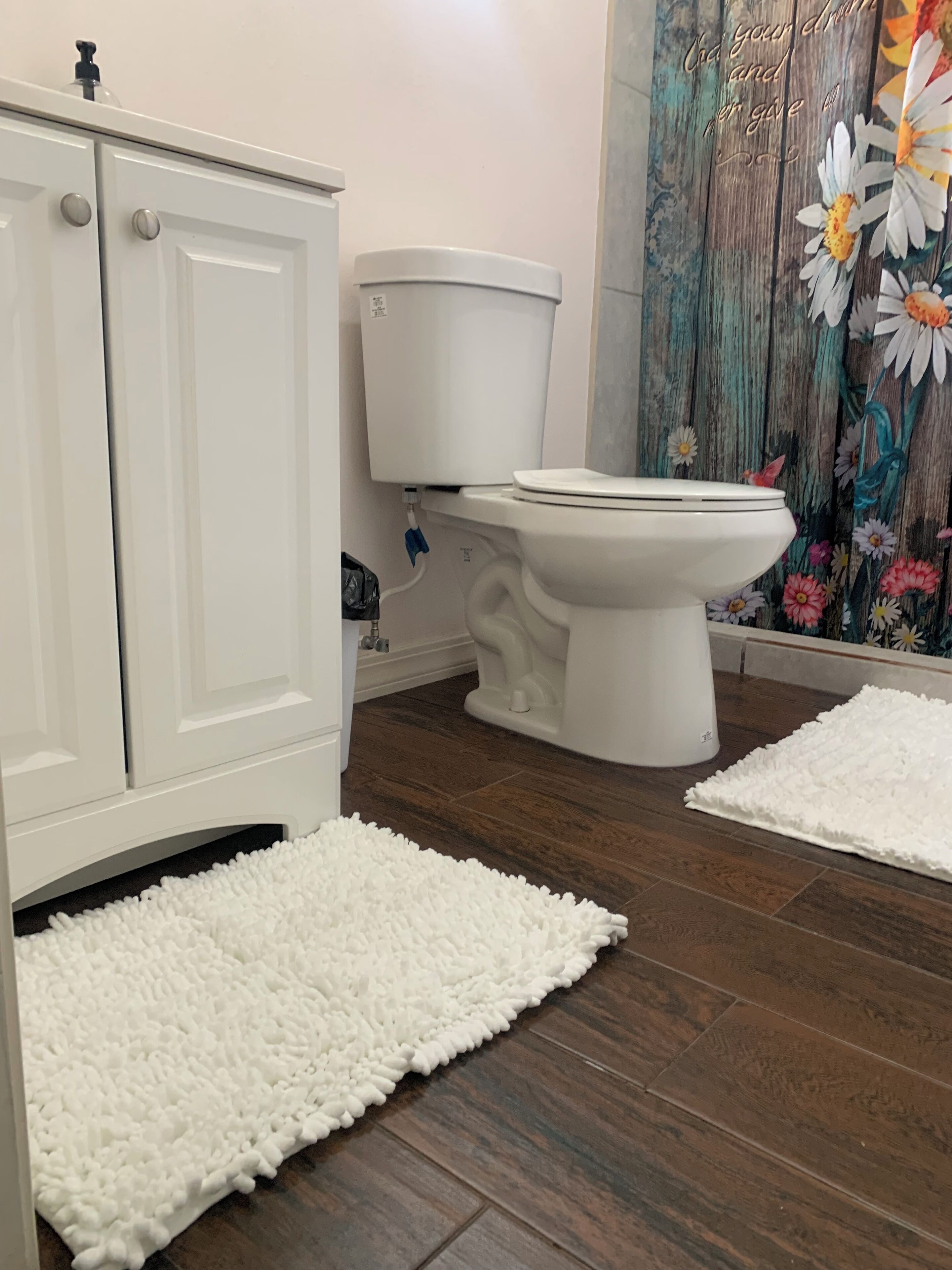 A bathroom with a white toilet, a white cabinet, and a floral curtain.
