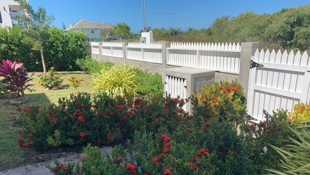 Un jardin agrémenté de plantes à fleurs rouges et bordé d’une clôture en bois peinte en blanc.