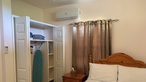 Une chambre à coucher comprenant un lit, une tête de lit en bois, une table de chevet avec une boîte de mouchoirs, une armoire et un appareil de climatisation.