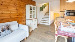 Una sala de estar acogedora con un sofá azul claro, una pared de madera, un armario blanco y una escalera que lleva a una cocina con muebles de madera y una estufa moderna.