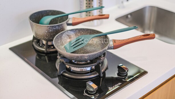 Une cuisine avec deux poêles sur la cuisinière, un évier et un porte-ustensiles en métal.