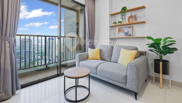 A modern living room with a grey sofa, a round wooden table, and a large window with a city view.