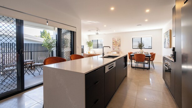 Una cocina moderna con una isla central, un comedor con sillas anaranjadas y un puerta corredera de vidrio que da a un patio exterior.