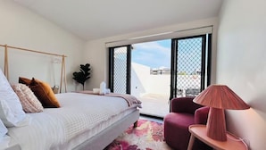 Un dormitorio moderno con una cama, una silla, una lámpara y un ventanal grande.