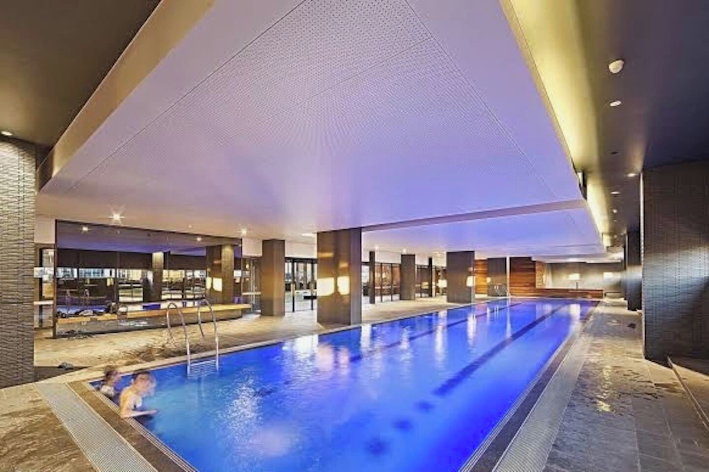A large indoor swimming pool with a clear view of the pool area, surrounded by modern architecture and a well-lit interior.