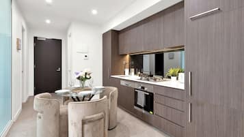 A modern kitchen with a dining area, featuring a glass table, cushioned chairs, and a built-in oven.
