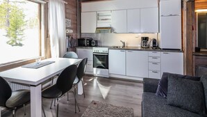 Una cocina compacta con armarios blancos, estufa y cafetera. Hay una mesa de comedor con sillas y un sofá en la sala de estar.