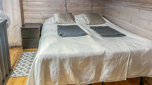 Una habitación pequeña y acogedora, con techo inclinado de madera, una cama individual con dos almohadas, una mesita de noche y una pequeña cómoda.