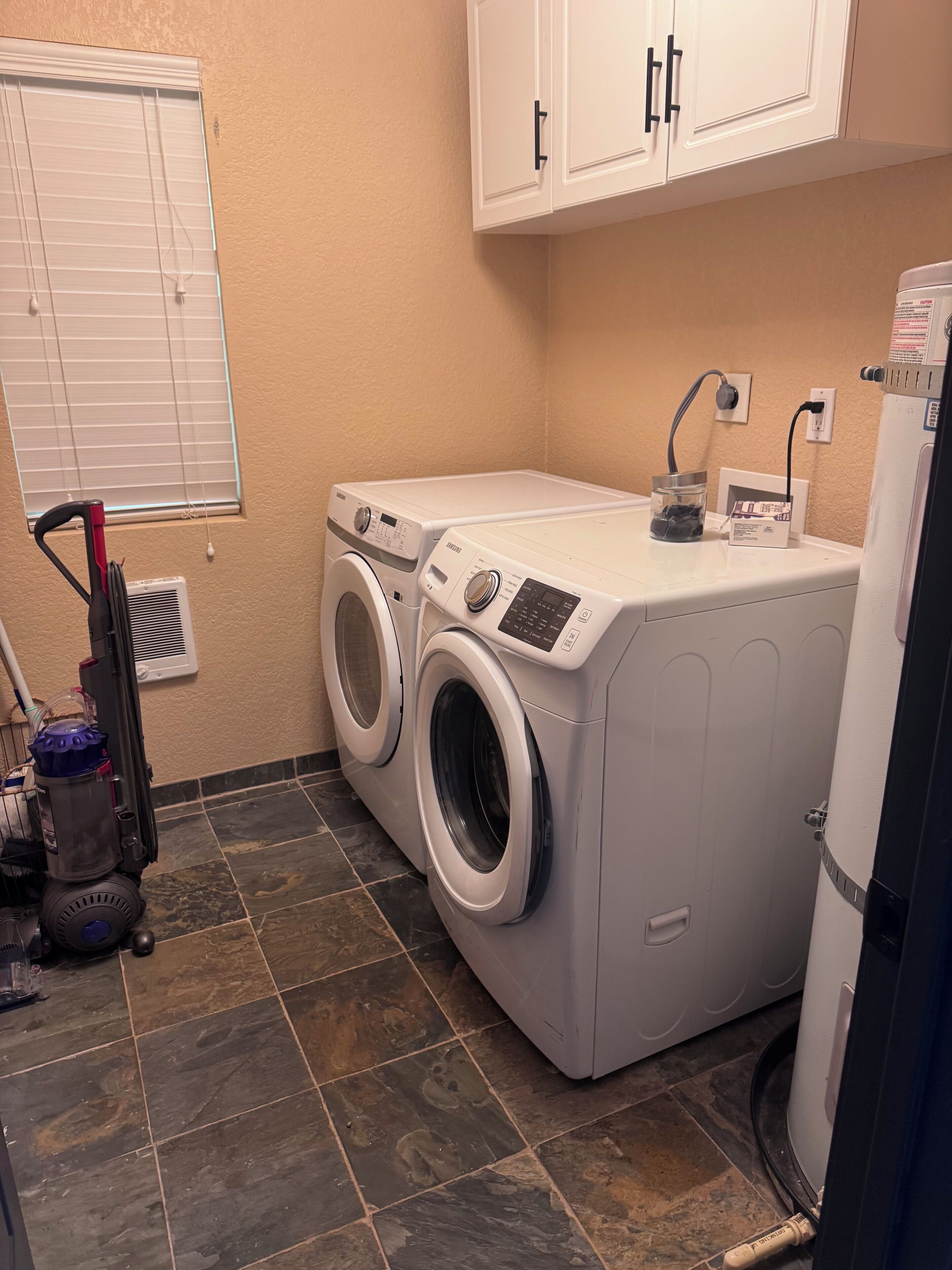 A laundry room with two front-loading washers, a vacuum cleaner, and a refrigerator.