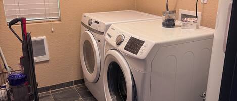 A laundry room with two front-loading washers, a vacuum cleaner, and a refrigerator.