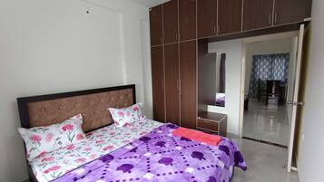 Quarto com uma cama, guarda-roupa, espelho e porta que dá para outro espaço.
