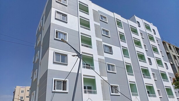 A multi-story residential building with balconies, a covered parking area, and a clear blue sky. - SAGAR NIWAS SARJAPUR (Bengaluru)