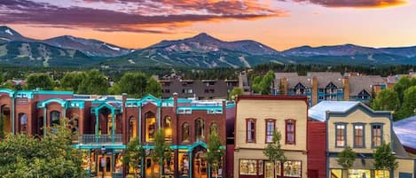 A street view of a town with historic buildings, a clear sky, and mountains in the background.