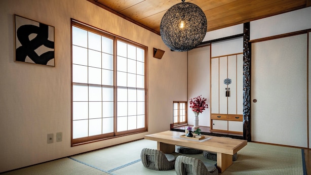 Een traditionele Japanse kamer met tatami vloeren, een houten tafel met kussens, een hanglamp en schuifdeuren.