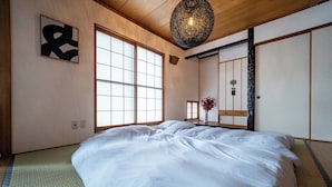 Een traditionele Japanse slaapkamer met tatami vloeren, een groot bed, schuifdeuren en een hanglamp.