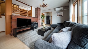 Een moderne woonkamer met een bakstenen open haard, een grote hoekbank, een flatscreen televisie en een houten plafondconstructie.