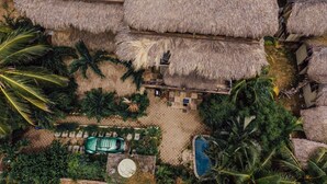 An aerial view of a resort with thatched-roof structures, a swimming pool, and lush tropical vegetation. - BeachfrontGuestHouse (5 Studios) (Puerto Escondido)